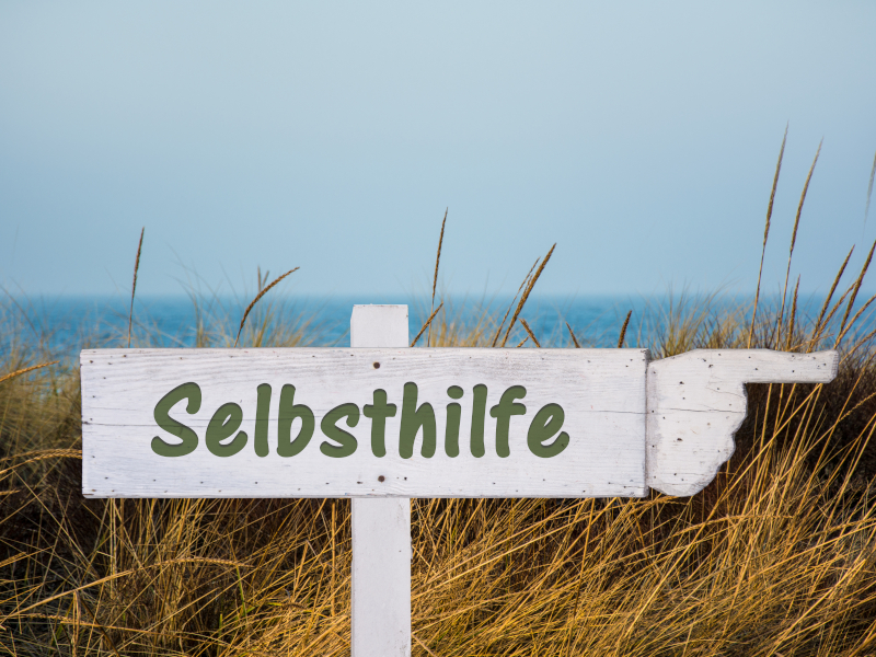 Schild mit der Aufschrift Selbsthilfe an einem Strand